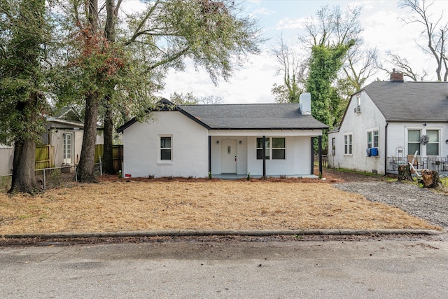 view of front of house with covered porch, fence, a chimney, and stucco siding