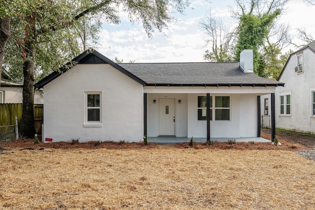 view of front of house featuring a porch, a shingled roof, fence, stucco siding, and a chimney