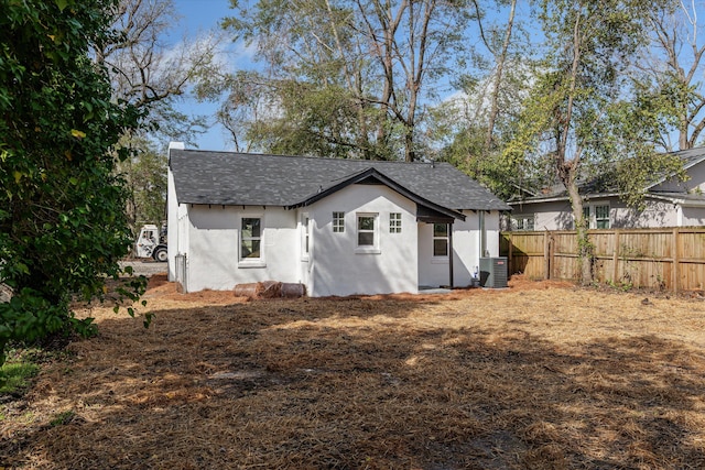 back of property with a shingled roof, stucco siding, fence, and central air condition unit