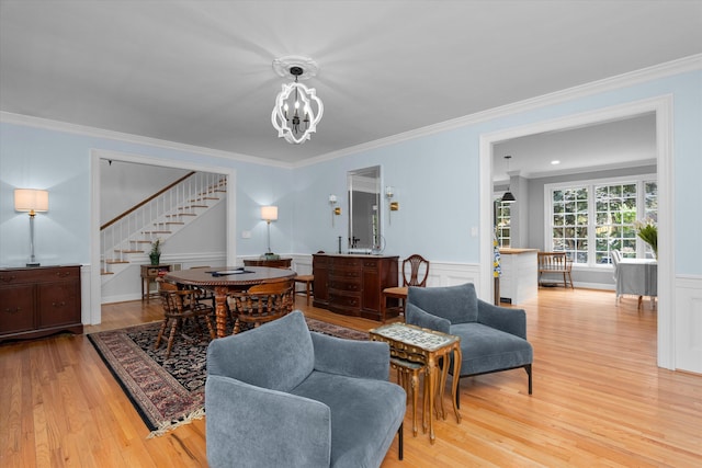 living area featuring ornamental molding, stairs, light wood-type flooring, a wainscoted wall, and a chandelier