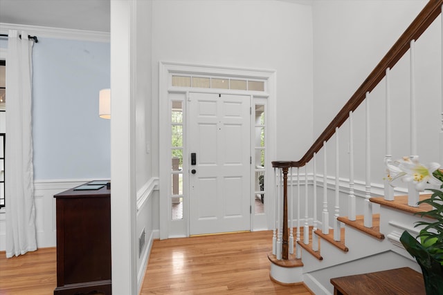 entrance foyer featuring stairway, a wainscoted wall, a decorative wall, and light wood-style flooring