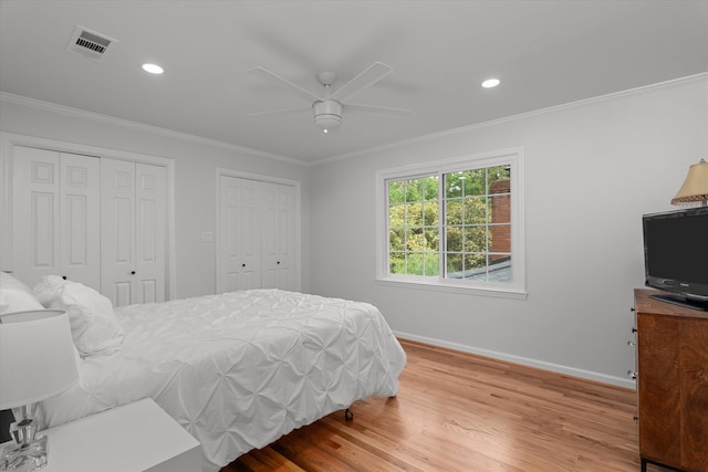 bedroom featuring multiple closets, baseboards, wood finished floors, visible vents, and ornamental molding