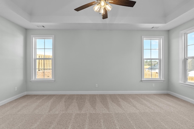 unfurnished room with carpet floors, a raised ceiling, a wealth of natural light, and ceiling fan