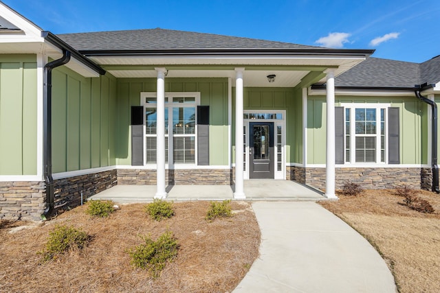 view of exterior entry featuring stone siding, covered porch, board and batten siding, and a shingled roof