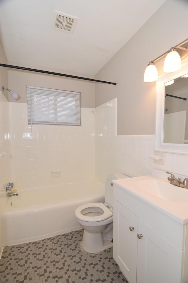 full bathroom featuring tiled shower / bath combo, toilet, tile walls, and vanity