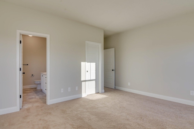 unfurnished bedroom with light carpet, ensuite bath, and baseboards