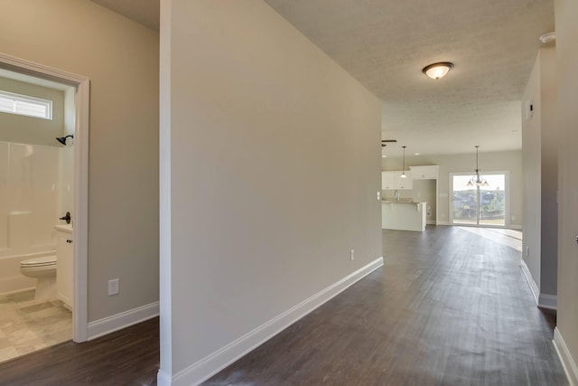 corridor featuring a chandelier, dark wood finished floors, and baseboards