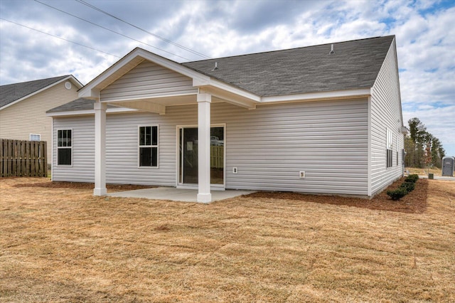 rear view of property featuring a lawn, fence, roof with shingles, and a patio area