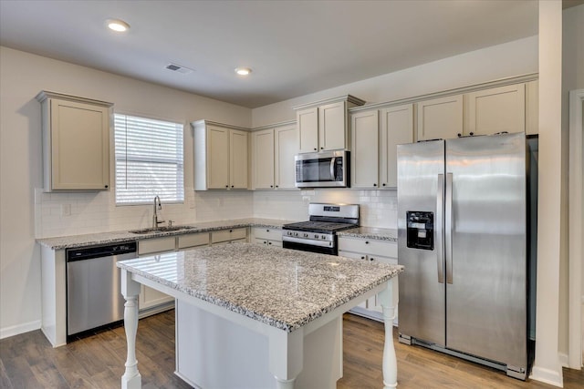 kitchen with light stone counters, a center island, visible vents, appliances with stainless steel finishes, and a sink