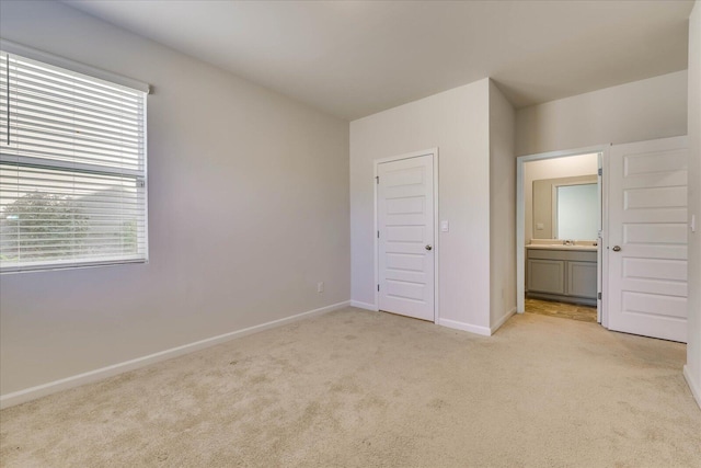 unfurnished bedroom with light carpet, a sink, baseboards, and ensuite bathroom