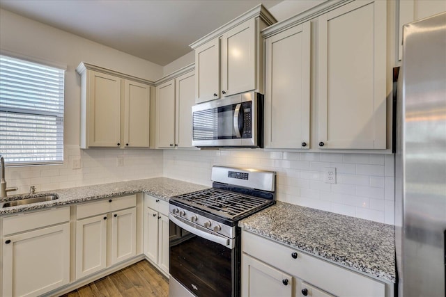 kitchen featuring appliances with stainless steel finishes, decorative backsplash, a sink, and light stone countertops