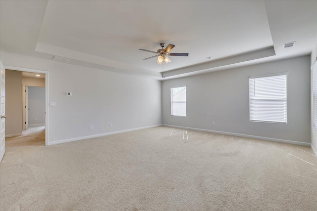 spare room with light carpet, baseboards, visible vents, and a tray ceiling