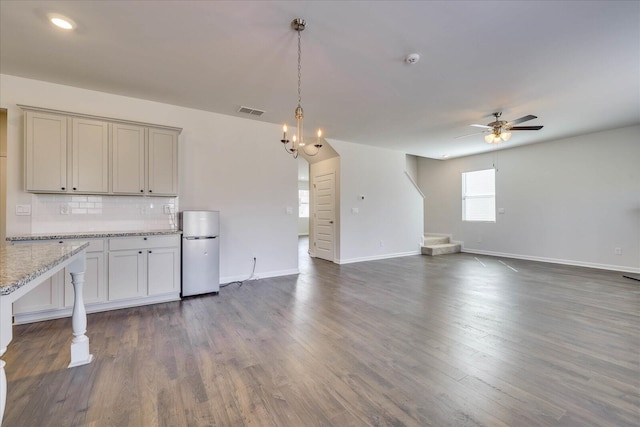 kitchen featuring light stone counters, dark wood-style flooring, tasteful backsplash, freestanding refrigerator, and open floor plan