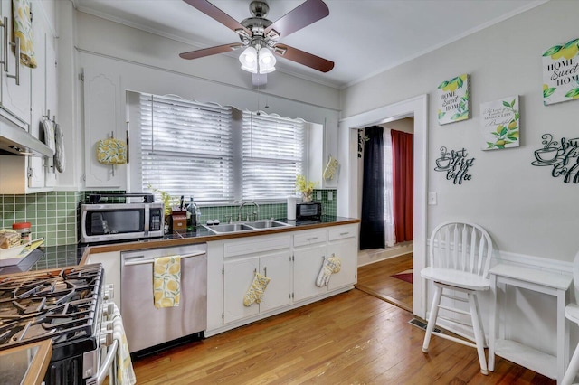 kitchen featuring sink, light wood-type flooring, appliances with stainless steel finishes, tasteful backsplash, and white cabinetry