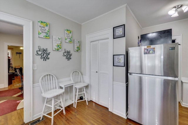 kitchen featuring hardwood / wood-style floors, stainless steel refrigerator, and crown molding