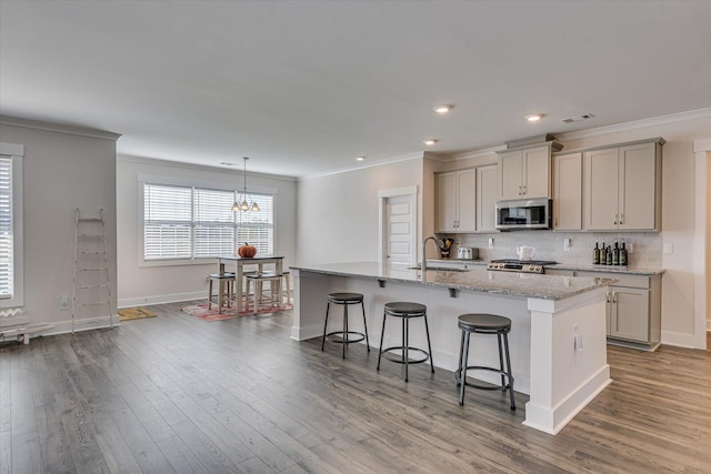 kitchen with gray cabinetry, sink, light stone counters, a breakfast bar, and a center island with sink