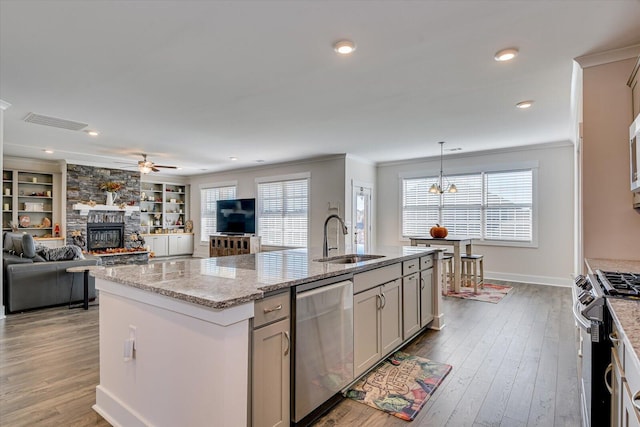 kitchen featuring built in shelves, stainless steel appliances, a kitchen island with sink, sink, and a fireplace