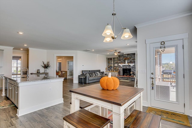 dining room featuring ceiling fan, sink, a stone fireplace, dark hardwood / wood-style floors, and ornamental molding