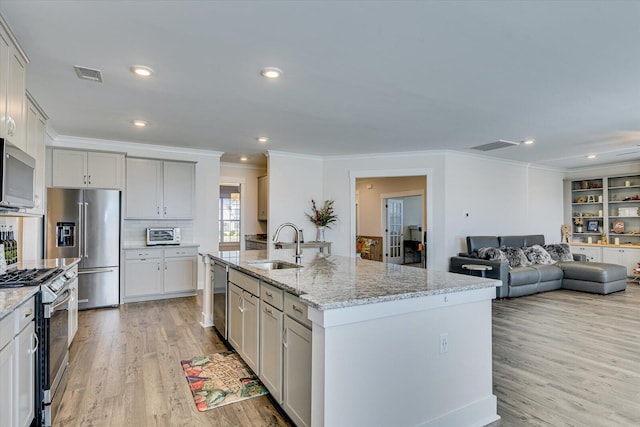 kitchen featuring light stone countertops, stainless steel appliances, a kitchen island with sink, sink, and light hardwood / wood-style flooring