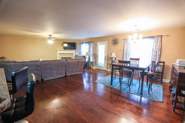 dining space featuring ceiling fan with notable chandelier, a fireplace, baseboards, and hardwood / wood-style floors