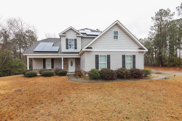 view of front of home with roof mounted solar panels, covered porch, a front yard, and stone siding