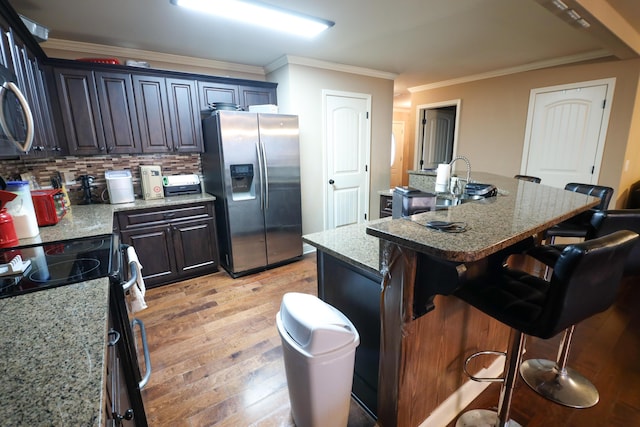 kitchen featuring light wood finished floors, a breakfast bar, black electric range, stainless steel fridge, and backsplash