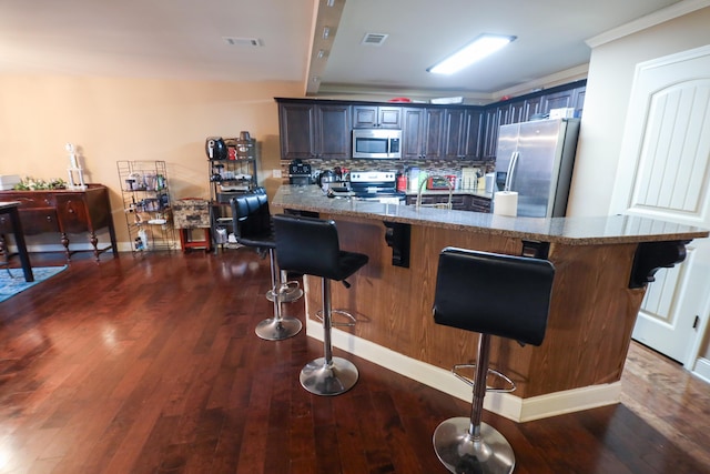 kitchen featuring visible vents, dark wood finished floors, stainless steel appliances, a kitchen breakfast bar, and backsplash