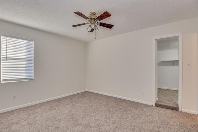 unfurnished bedroom with a spacious closet, a textured ceiling, light carpet, and ceiling fan