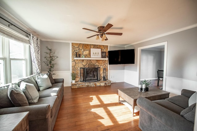 living room with ceiling fan, a stone fireplace, wood-type flooring, and ornamental molding