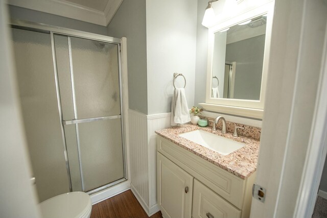 bathroom featuring vanity, a shower with door, crown molding, hardwood / wood-style floors, and toilet