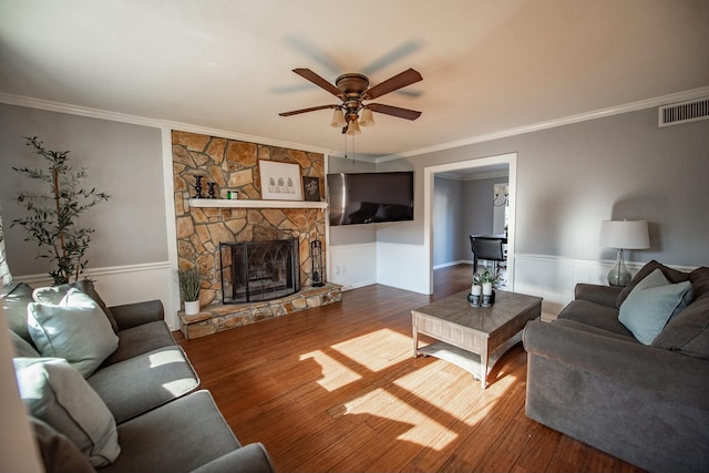 living room featuring wood-type flooring, a stone fireplace, ceiling fan, and crown molding