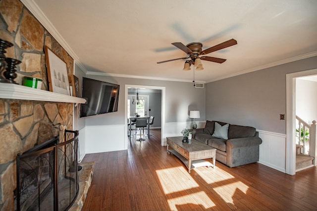 living room featuring dark hardwood / wood-style flooring, a stone fireplace, ceiling fan, and crown molding