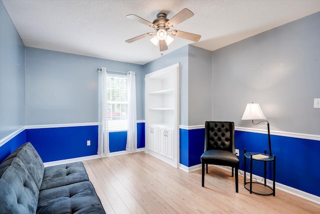 living area featuring ceiling fan, baseboards, wood finished floors, and a textured ceiling