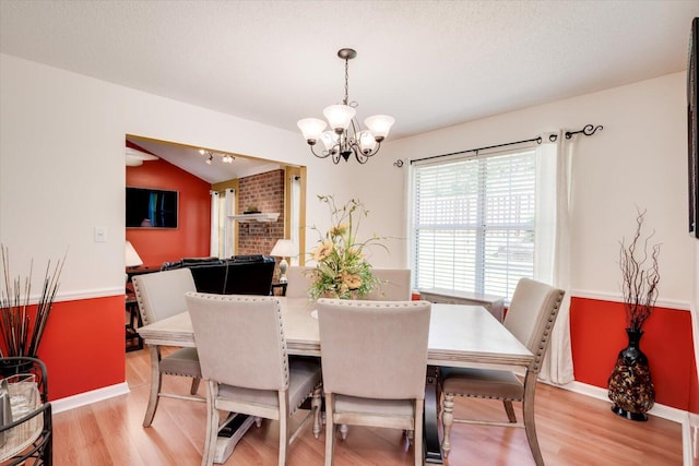 dining space featuring baseboards, vaulted ceiling, an inviting chandelier, a textured ceiling, and light wood-style floors