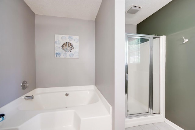 bathroom featuring tile patterned floors, a bath, a shower stall, and a textured ceiling