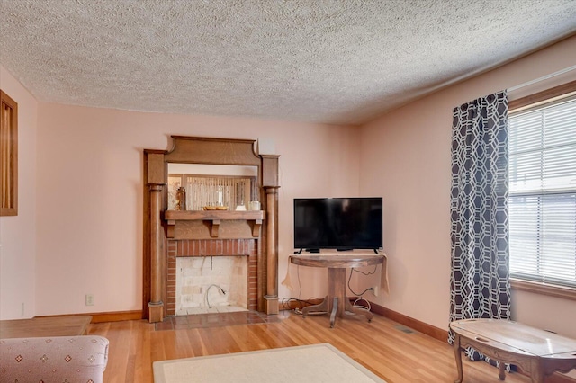 living room featuring a brick fireplace, a textured ceiling, and light hardwood / wood-style flooring