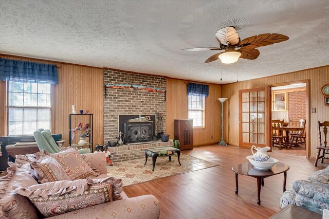 living room with light hardwood / wood-style floors, a wood stove, a wealth of natural light, and ceiling fan