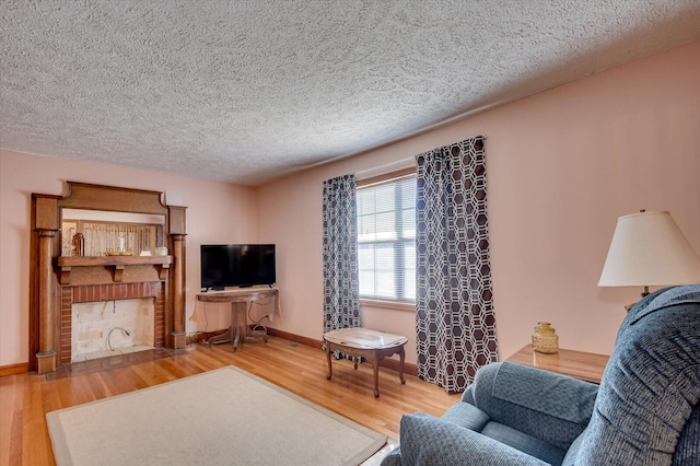 living room featuring wood-type flooring, a textured ceiling, and a brick fireplace