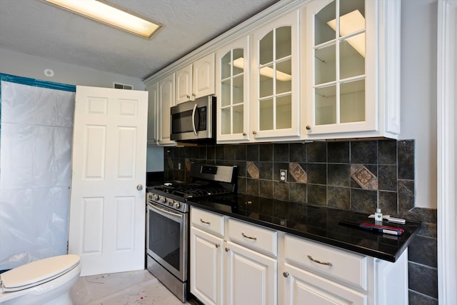 kitchen featuring stainless steel appliances, visible vents, white cabinetry, backsplash, and glass insert cabinets