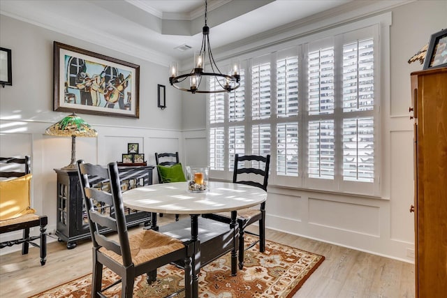 dining area featuring a tray ceiling, ornamental molding, light wood-style floors, a decorative wall, and a notable chandelier