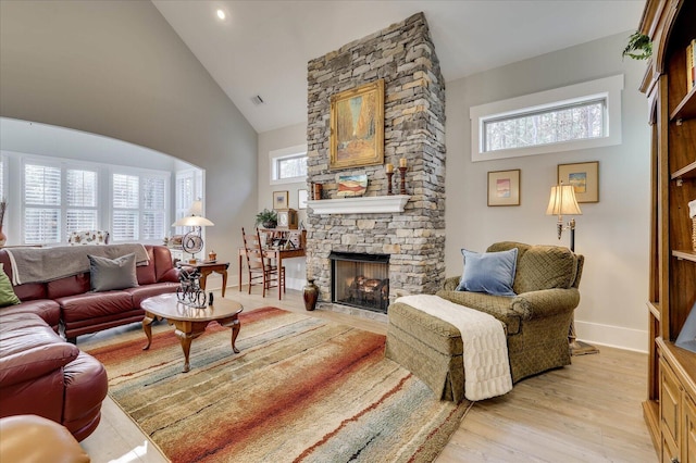 living area featuring arched walkways, high vaulted ceiling, a stone fireplace, and light wood finished floors