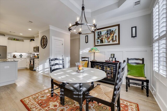 dining space with visible vents, a notable chandelier, light wood-style flooring, ornamental molding, and a decorative wall