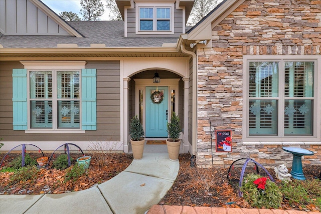 doorway to property with stone siding, roof with shingles, and board and batten siding