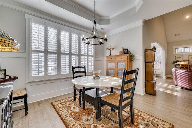 dining space with crown molding, light wood-type flooring, arched walkways, a decorative wall, and a raised ceiling