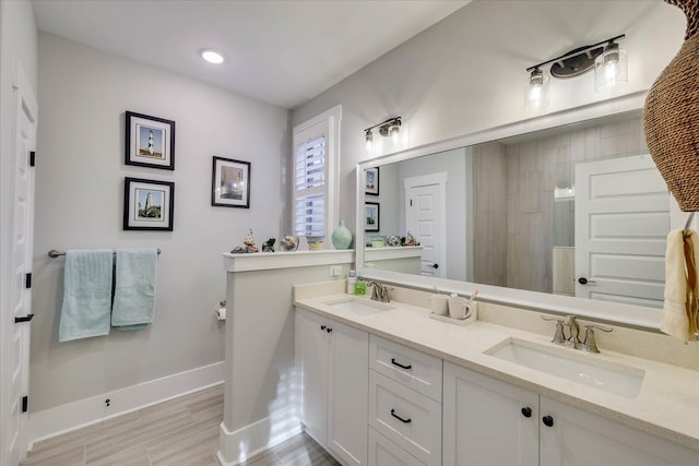 bathroom featuring double vanity, tiled shower, baseboards, and a sink