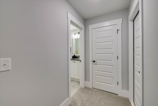 hallway featuring a sink, baseboards, and light carpet