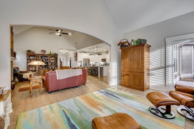 living area featuring ceiling fan, arched walkways, light wood finished floors, and high vaulted ceiling