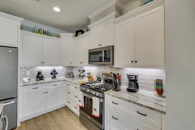 kitchen with tasteful backsplash, crown molding, appliances with stainless steel finishes, light wood-style floors, and white cabinets