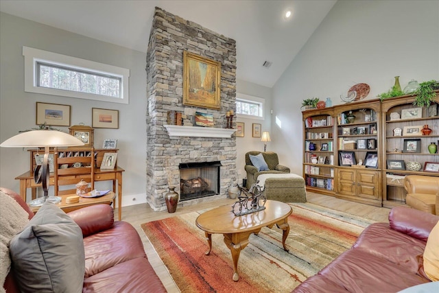 living area with a stone fireplace, visible vents, light wood-type flooring, and high vaulted ceiling