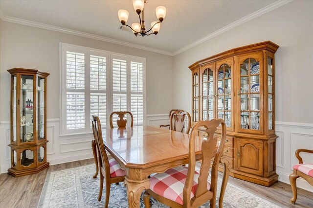 dining room featuring light wood finished floors, a wainscoted wall, crown molding, and an inviting chandelier